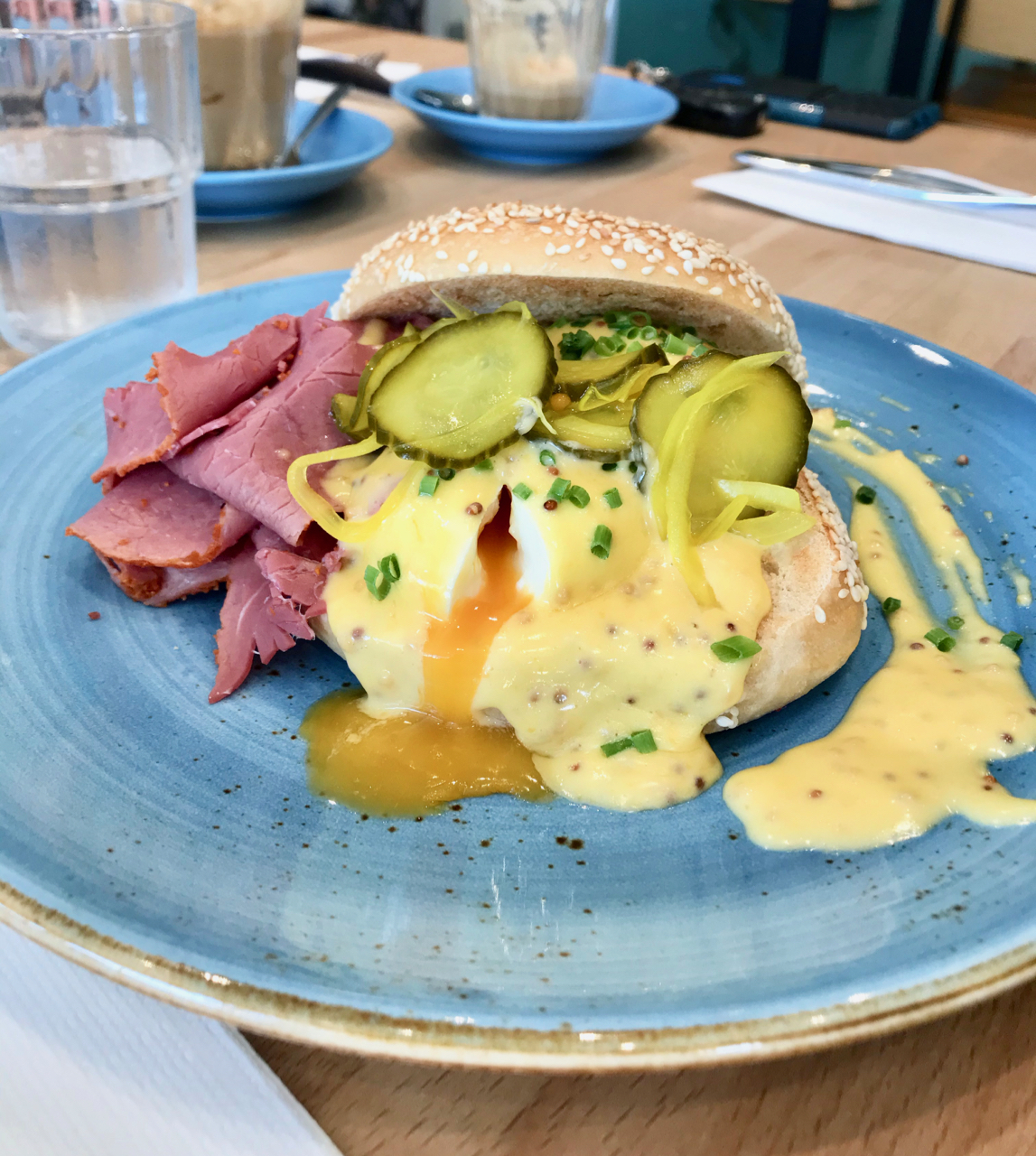 Eggs benedict served with shaved pastrami and pickles on a bagel